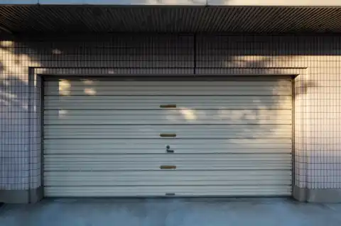 Single tan roll-up garage door set into a tiled residential building facade